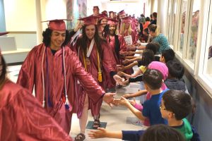 WHS seniors in graduation cap and gowns walking down a hallway giving 5's to elementary students