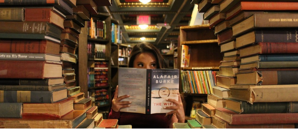 person reading a book in the middle of stacks of books