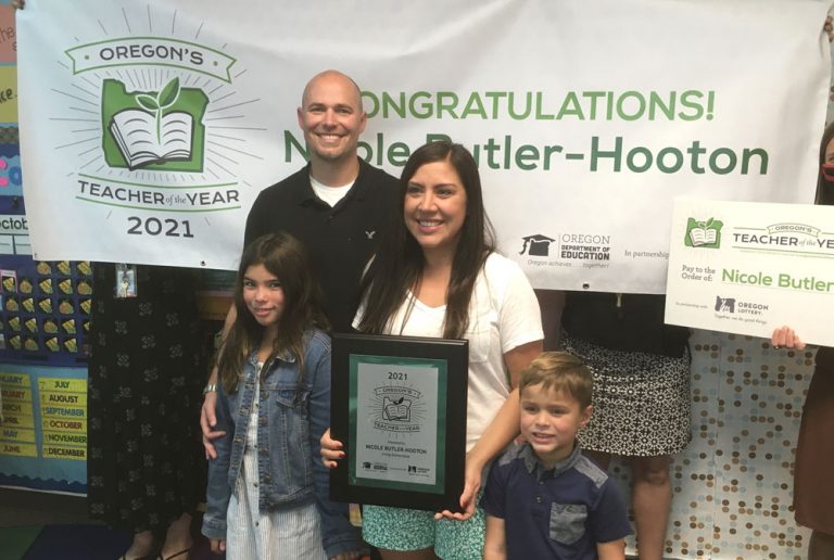 Teacher of the Year Nicole standing with her husband and two children in front of a banner