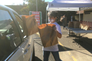 student handing bags of groceries to someone in a car