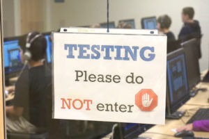 sign in classroom window that reads "testing, please do not enter" with a hand inside a stop sign
