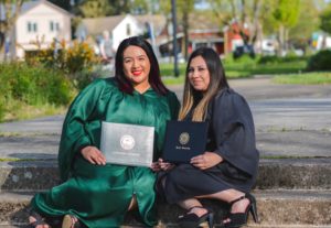 Ana and Adriana sitting down on a step with their diplomas