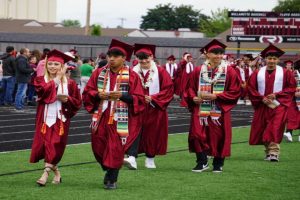 a group of students in cap and gown walking across a football field